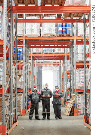 Group of large contemporary warehouse workers in gloves, respirators and uniform Group of large contemporary warehouse workers in gloves, respirators and uniform 71062742