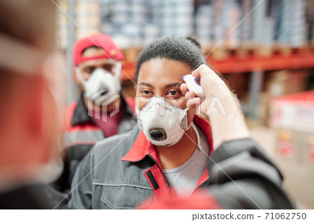 Contemporary factory worker of warehouse having her temperature measured Contemporary factory worker of warehouse having her temperature measured 71062750