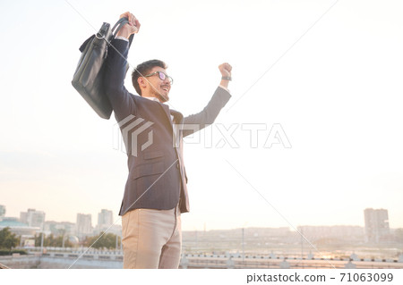 Young excited businessman with black leather handbag expressing triumph 71063099