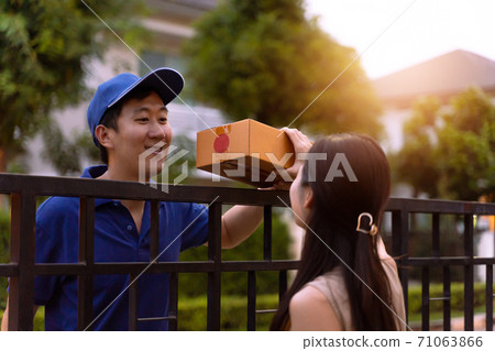 Asian delivery man in blue shirt sending parcel box to home while young woman receiving a package in front of custoomer house Asian delivery man in blue shirt sending parcel box to home while young woman receiving a package in front of custoomer house 71063866