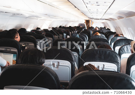 Interior of a plane with passengers on their seats . Interior of a plane with passengers on their seats . 71066430