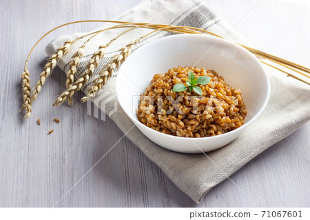 Spelt porridge in a bowl with basil. White wooden background. Spelt porridge in a bowl with basil. White wooden background. 71067601