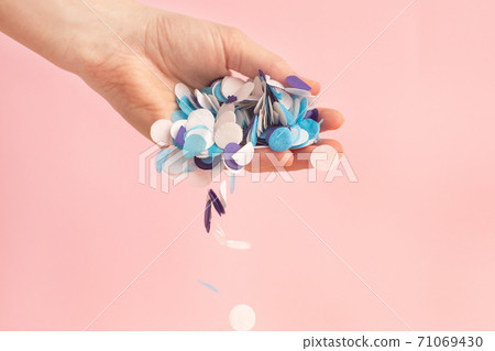 White, lilac and blue confetti in a woman's hand on a pink background White, lilac and blue confetti in a woman's hand on a pink background 71069430