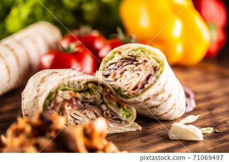 Kebab filled tortilla wraps on a table with vegetables in teh background Kebab filled tortilla wraps on a table with vegetables in teh background 71069497