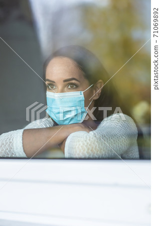 Social isolation during qurantine impacting the depressive mood of a woman sitting behind the window at home 71069892