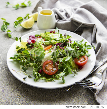 Fresh green mixed salad bowl with tomatoes and microgreens on concrete background. Fresh green mixed salad bowl with tomatoes and microgreens on concrete background. 71070197