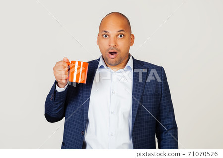 Portrait of astonished young African American businessman guy, holding a cup of coffee in his hand 71070526
