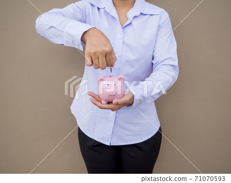 Businesswomen hand putting gold coin into pink piggy bank on brown cement wall background, Saving money for future plan and retirement fund concept Businesswomen hand putting gold coin into pink piggy bank on brown cement wall background, Saving money for future plan and retirement fund concept 71070593