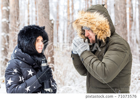 Season and walk concept - Happy couple drinking hot tea in winter forest 71073576