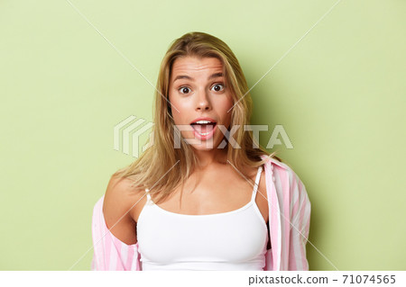 Close-up of attractive blond woman in pink shirt, looking surprised, open mouth fascinated, standing over green background Close-up of attractive blond woman in pink shirt, looking surprised, open mouth fascinated, standing over green background 71074565