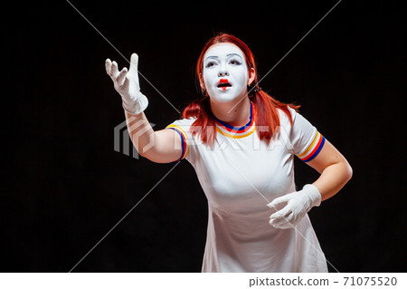 Portrait of female mime artist, isolated on black background. Young woman pretends playing tennis, pitching the ball Portrait of female mime artist, isolated on black background. Young woman pretends playing tennis, pitching the ball 71075520