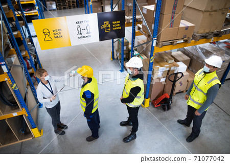 Group of workers with face mask in warehouse, coronavirus and temperature measuring concept. Group of workers with face mask in warehouse, coronavirus and temperature measuring concept. 71077042