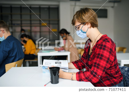 Young student with face mask at desk at college or university, coronavirus concept. 71077411