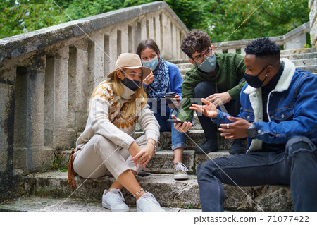 Group of young people outdoors in town, using smartpone. Coronavirus concept. 71077422