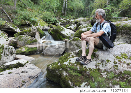 Man sitting on a stone near a mountain river Man sitting on a stone near a mountain river 71077584