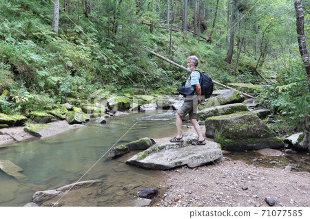 Man standing on a stone near a mountain river Man standing on a stone near a mountain river 71077585