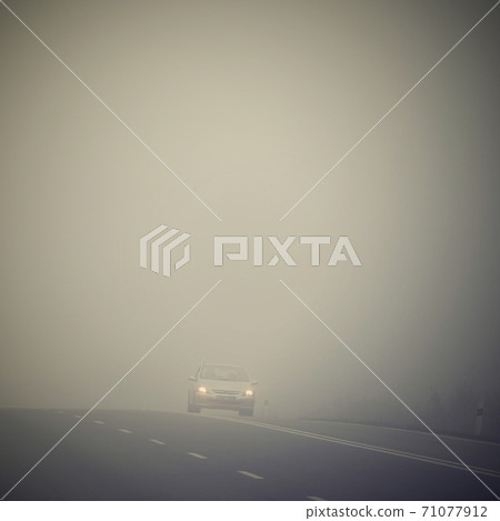 Car on the road in the fog. Autumn landscape - dangerous road traffic in winter season. 71077912