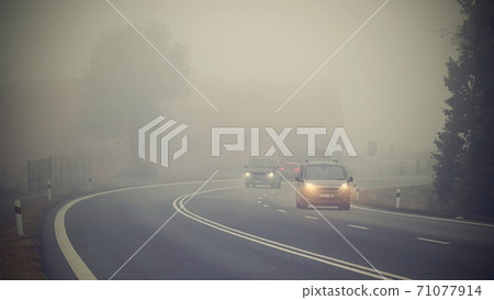 Car on the road in the fog. Autumn landscape - dangerous road traffic in winter season. Car on the road in the fog. Autumn landscape - dangerous road traffic in winter season. 71077914