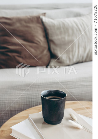 Books, dry bunny tail grass and black cup of coffee on round wooden table. Blurred beige sofa background with linen cushions. Hygge, cozy lifestyle concept. Scandinavian interior. Vertical. Books, dry bunny tail grass and black cup of coffee on round wooden table. Blurred beige sofa background with linen cushions. Hygge, cozy lifestyle concept. Scandinavian interior. Vertical. 71078226