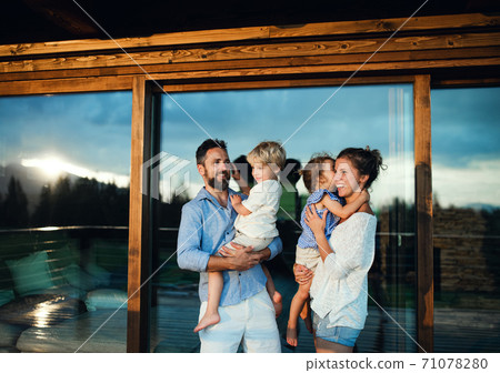 Family with small children standing by wooden cabin, holiday in nature concept. Family with small children standing by wooden cabin, holiday in nature concept. 71078280
