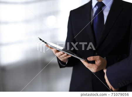 Business people use a tablet computer for discussion of their new project, standing in a modern office. Unknown businessman or male entrepreneur with a colleague at workplace. Teamwork and partnership Business people use a tablet computer for discussion of their new project, standing in a modern office. Unknown businessman or male entrepreneur with a colleague at workplace. Teamwork and partnership 71079056