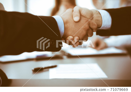 Business people shaking hands at meeting while theirs colleagues clapping and applauding. Group of unknown businessmen and women in modern white office. Success teamwork, partnership and handshake Business people shaking hands at meeting while theirs colleagues clapping and applauding. Group of unknown businessmen and women in modern white office. Success teamwork, partnership and handshake 71079669