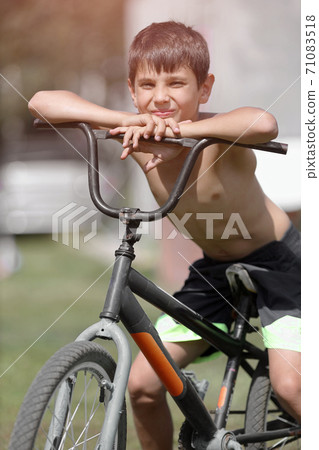 A child with an old Bicycle on the street. A white boy sits on an outdated Bicycle on a summer day.  71083518