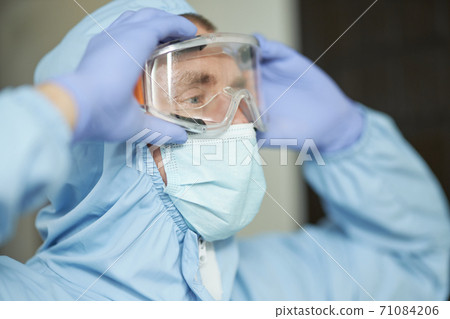 Sanitary worker in mask adjusting safety glasses 71084206