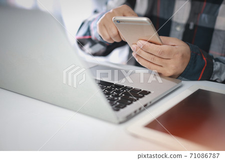 Man hands sitting and using smartphone and computer on table for online payment or shopping online. Man hands sitting and using smartphone and computer on table for online payment or shopping online. 71086787