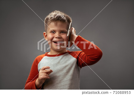 A little caucasian boy with a short haircut. Joyful communicates on the phone. On a gray background 71088953
