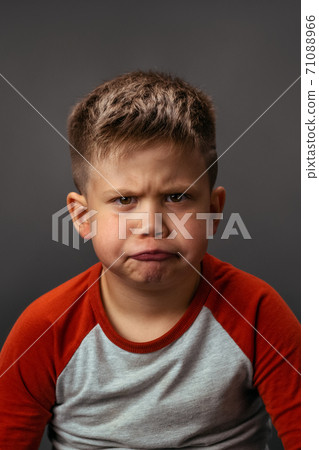Little boy is naughty and grimaces with displeasure. Disgruntled child shows his emotions. Studio portrait on gray background Little boy is naughty and grimaces with displeasure. Disgruntled child shows his emotions. Studio portrait on gray background 71088966