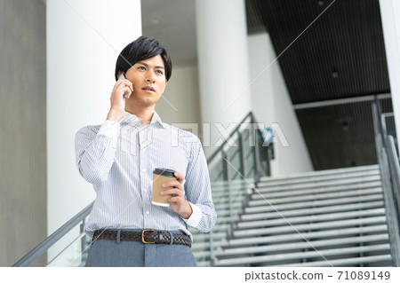 A young man talking on a smartphone over a drink in the office lobby 71089149