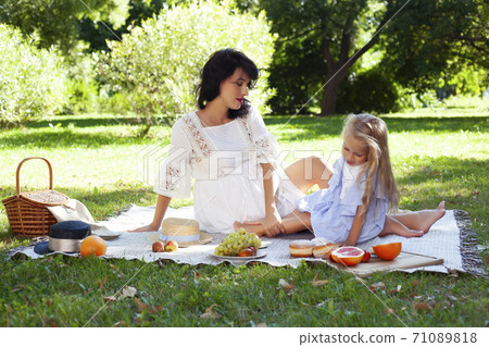 young pretty pregnant brunette woman having fun with her daughter on picnic on green grass in park, lifestyle people concept 71089818