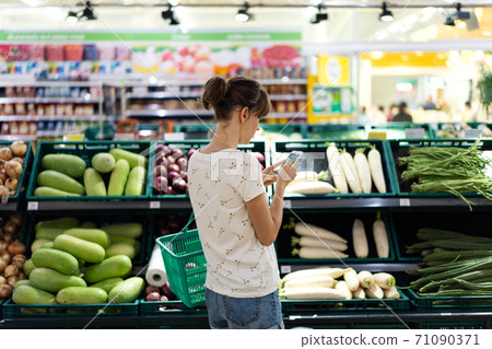 Woman using mobile phone while shopping in supermarket 71090371