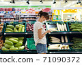 Young woman with face mask using mobile phone and buying groceries in the supermarket 71090372