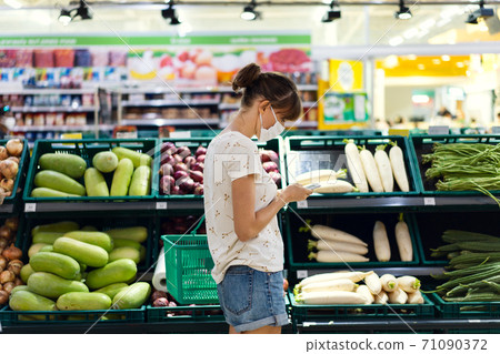 Young woman with face mask using mobile phone and buying groceries in the supermarket Young woman with face mask using mobile phone and buying groceries in the supermarket 71090372