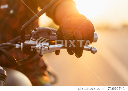 Macro left hand of motorcyclist wearing riding glove on the clutch. Outdoor shooting on the road with copy space 71090741
