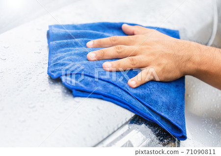 Hand holding blue cloth to cleaning wet body of modern car. Outdoor shooting in raining day. 71090811