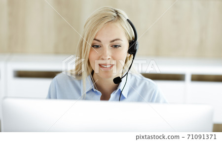 Blonde business woman sitting and communicated by headset in call center office. Concept of telesales business or home office occupation Blonde business woman sitting and communicated by headset in call center office. Concept of telesales business or home office occupation 71091371