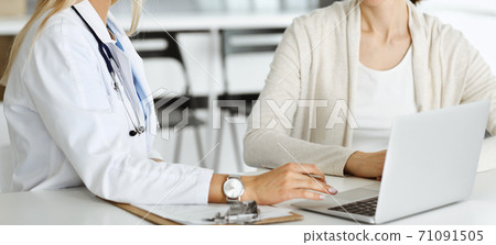 Unknown woman-doctor sitting and communicating with female patient. Physician checks medical history record and exam results, close-up. Healthcare concept 71091505