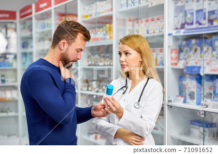 young helpful female druggist dealing with a male customer, explaining a prescription 71091652
