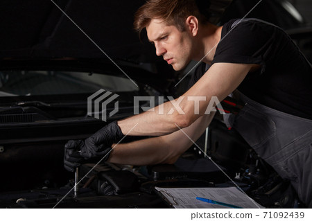 professional car mechanic is examining engine under the hood at auto repair shop 71092439