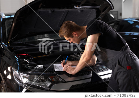 professional car mechanic is examining engine under the hood at auto repair shop 71092452