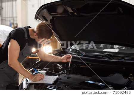 handsome caucasian guy is making notes while repairing hood of car 71092453
