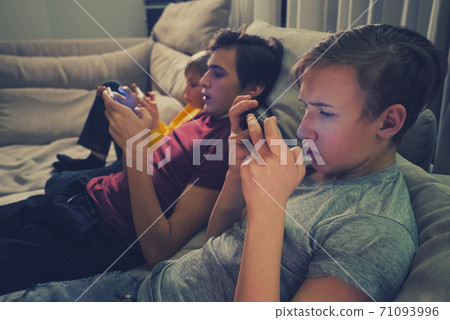 Three boys spending time in a social network using mobile phones. Children with smartphones at home. White kids using cell phones for gaming. People and social media concept Three boys spending time in a social network using mobile phones. Children with smartphones at home. White kids using cell phones for gaming. People and social media concept 71093996