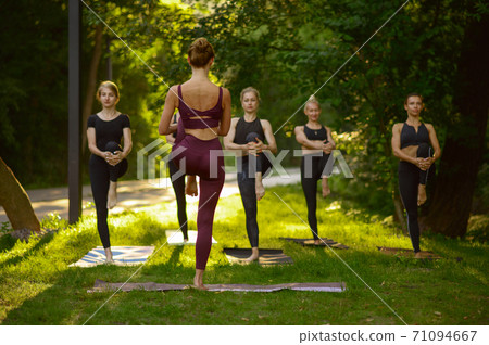 Women sits in yoga pose on grass, group training 71094667