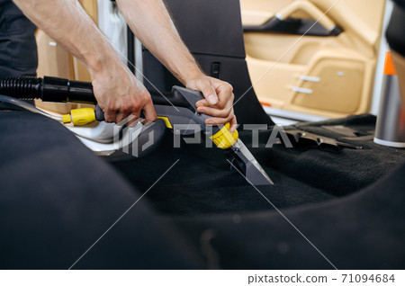 Worker cleans car interior with vacuum cleaner 71094684