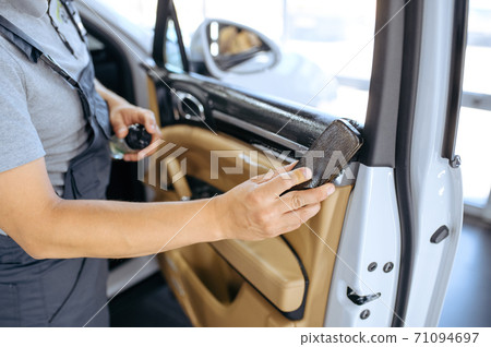 Worker with brush wipes car door trim, detailing 71094697