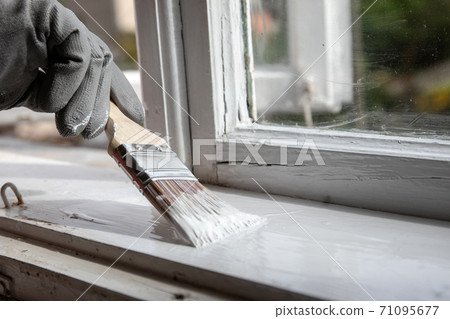Painting old wooden window with white color. Brush in hand with grey glove 71095677