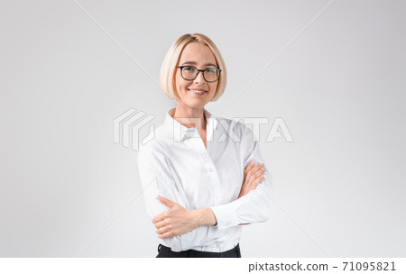Smiling female entrepreneur in formal clothes and glasses posing with crossed arms on light grey studio background Smiling female entrepreneur in formal clothes and glasses posing with crossed arms on light grey studio background 71095821
